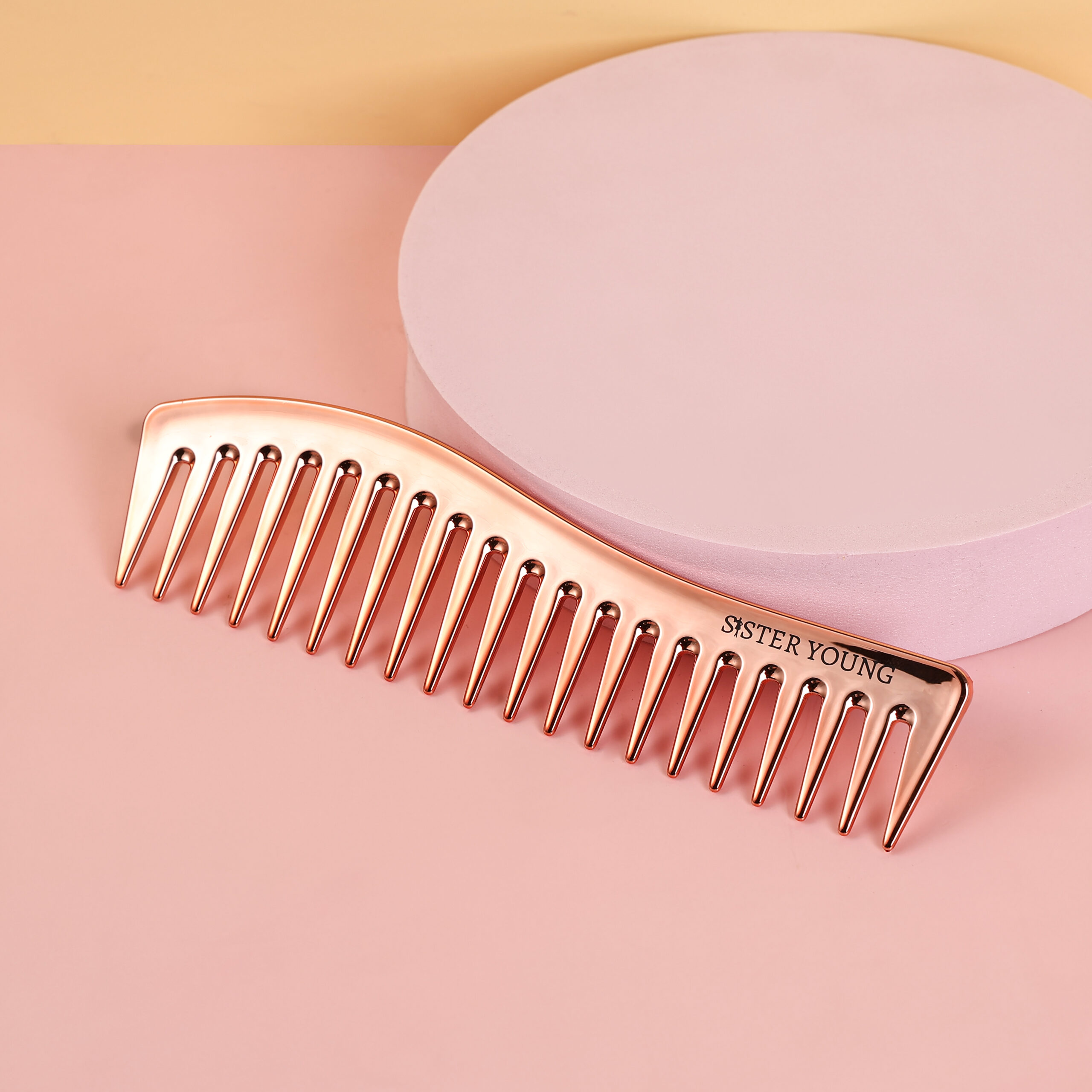 Grzebień Zuri Rose Gold ułożony ukośnie na różowo-brzoskwiniowym tle