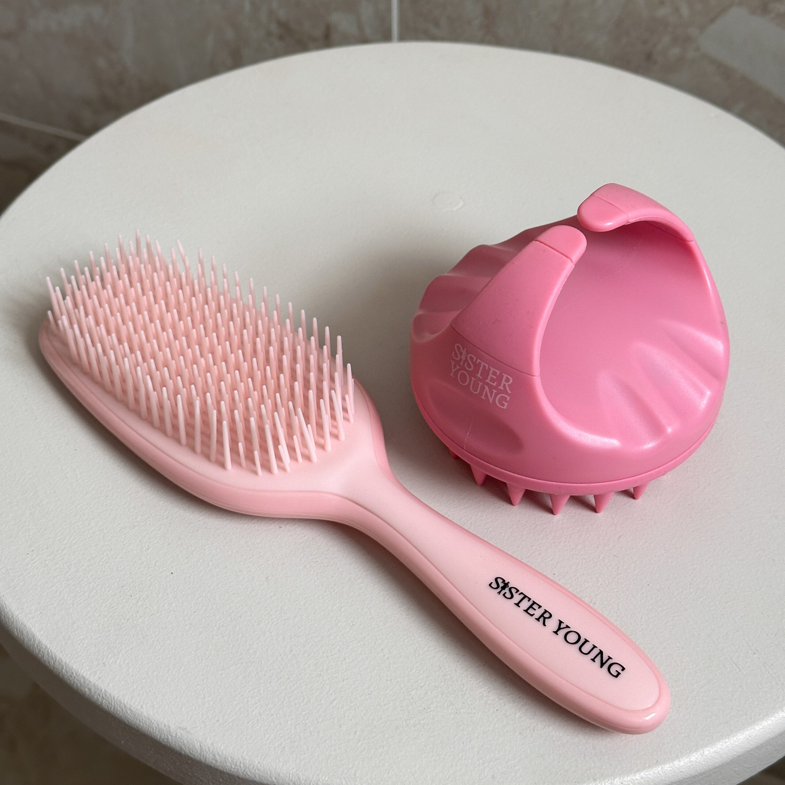 Szczotka do włosów Sister Young AYLA Pastel Peach obok różowego masażera skóry głowy AURA Pink.