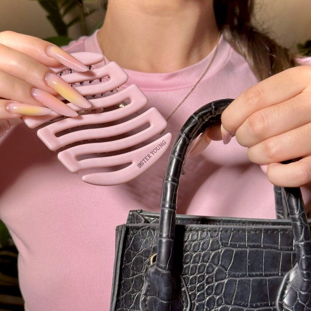 Różowa mini szczotka MILA Pocket BV trzymana w dłoni obok czarnej torebki
