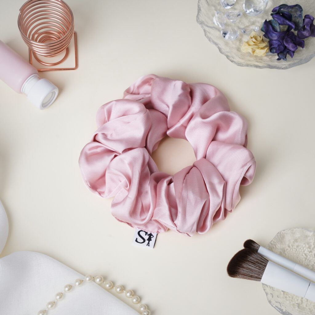 Różowa gumka LILU Pink na jasnym blacie, obok pędzli do makijażu i biżuterii.