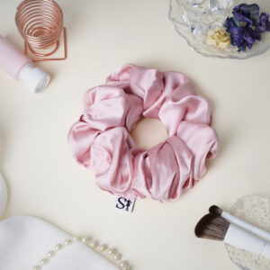 Różowa gumka LILU Pink na jasnym blacie, obok pędzli do makijażu i biżuterii.