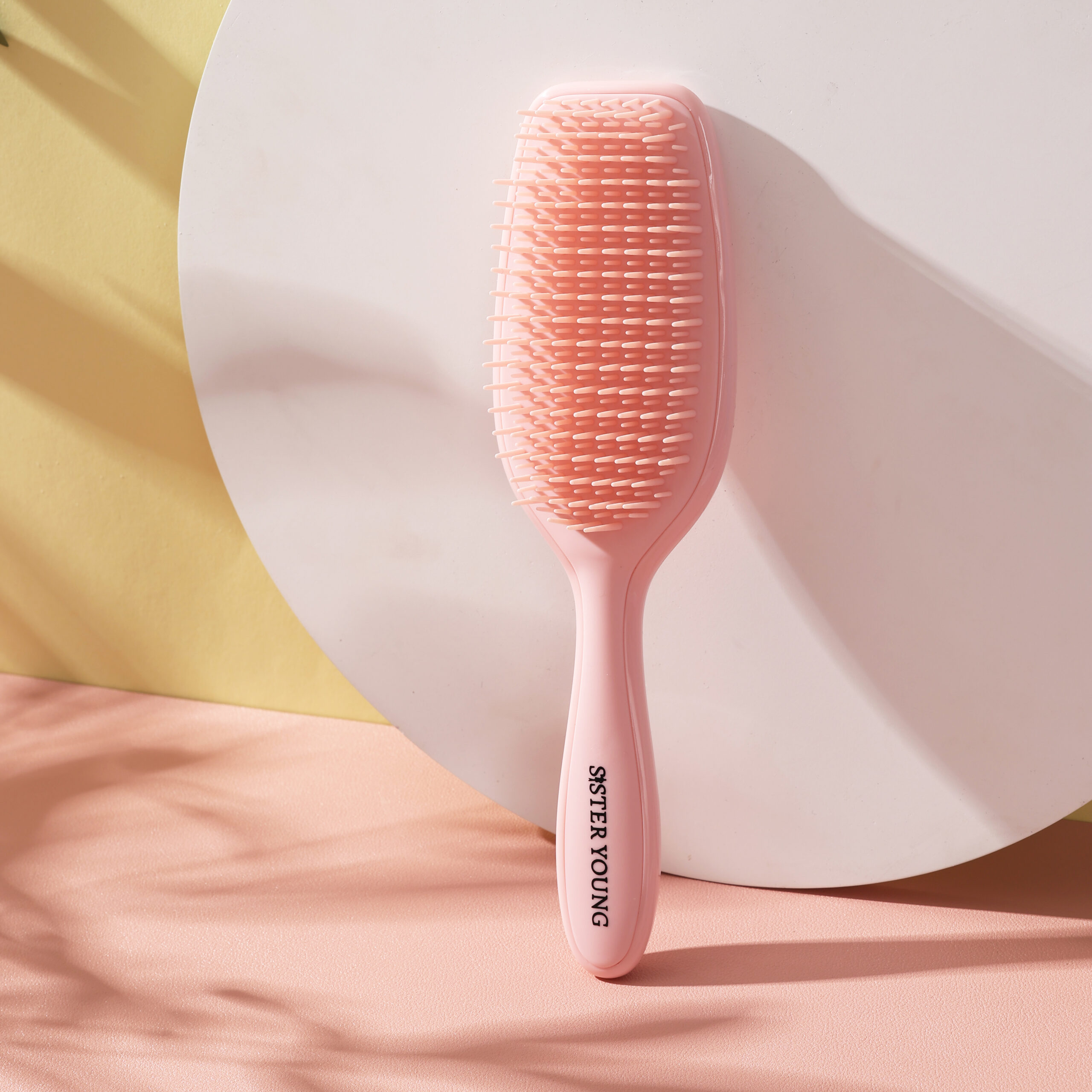 Szczotka do włosów Sister Young AYLA Pastel Peach ustawiona pionowo na tle jasnych dekoracji i brzoskwiniowej tkaniny.