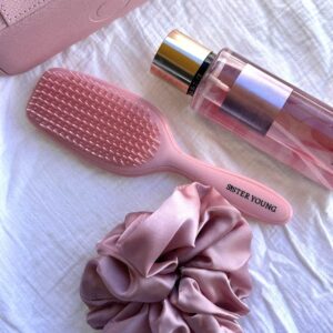 Szczotka Sister Young AYLA Pastel Peach obok gumki scrunchie i butelki kosmetyku na jasnej tkaninie.