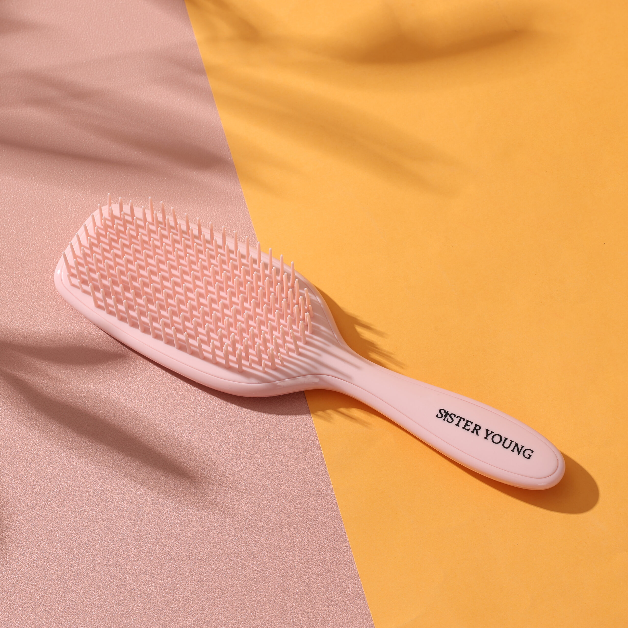 Szczotka do włosów Sister Young AYLA Pastel Peach ułożona na różowej i żółtej tkaninie.