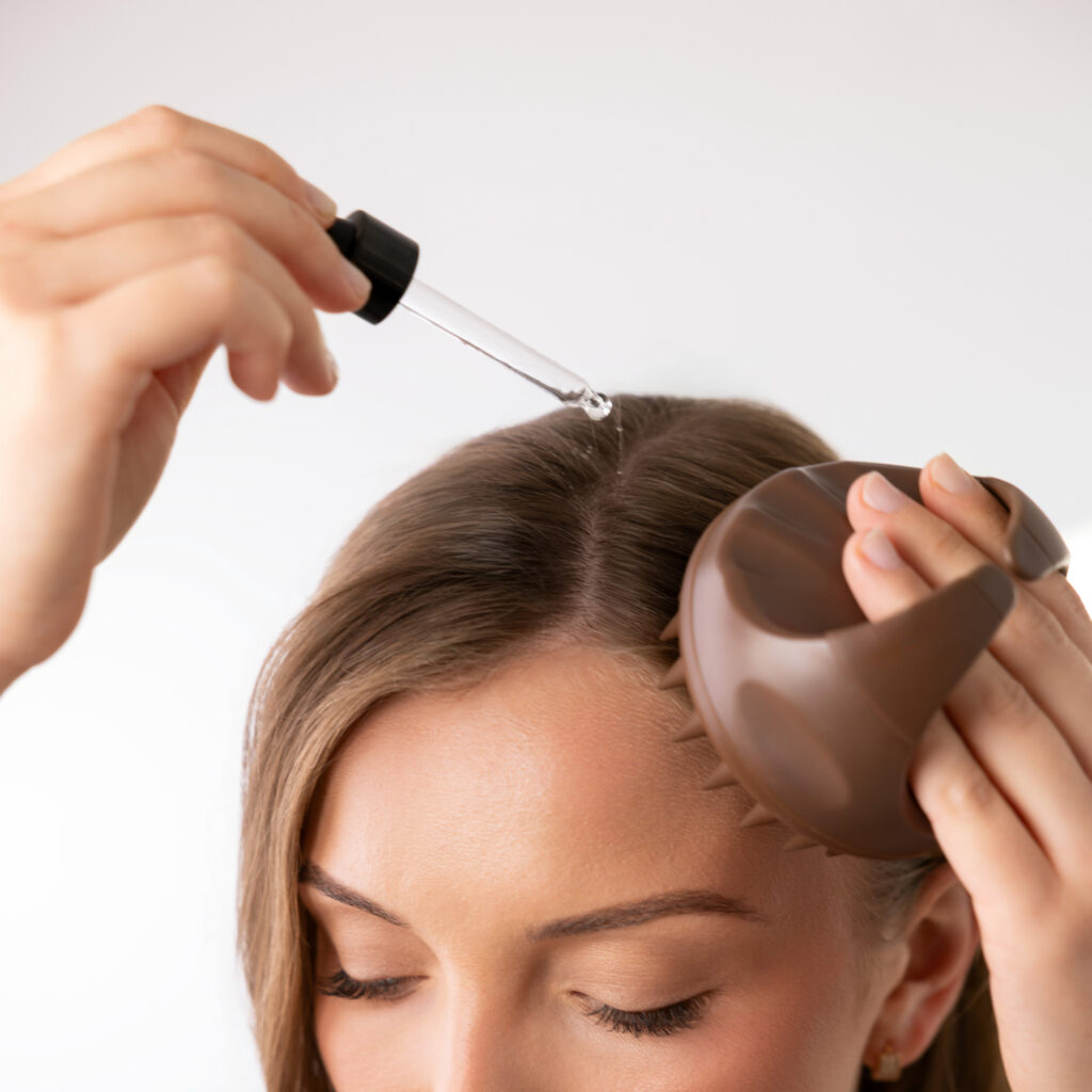 Kobieta nakładająca serum na skórę głowy ciemnobrązowym masażerem Sister Young AURA Chocolate Coffee.