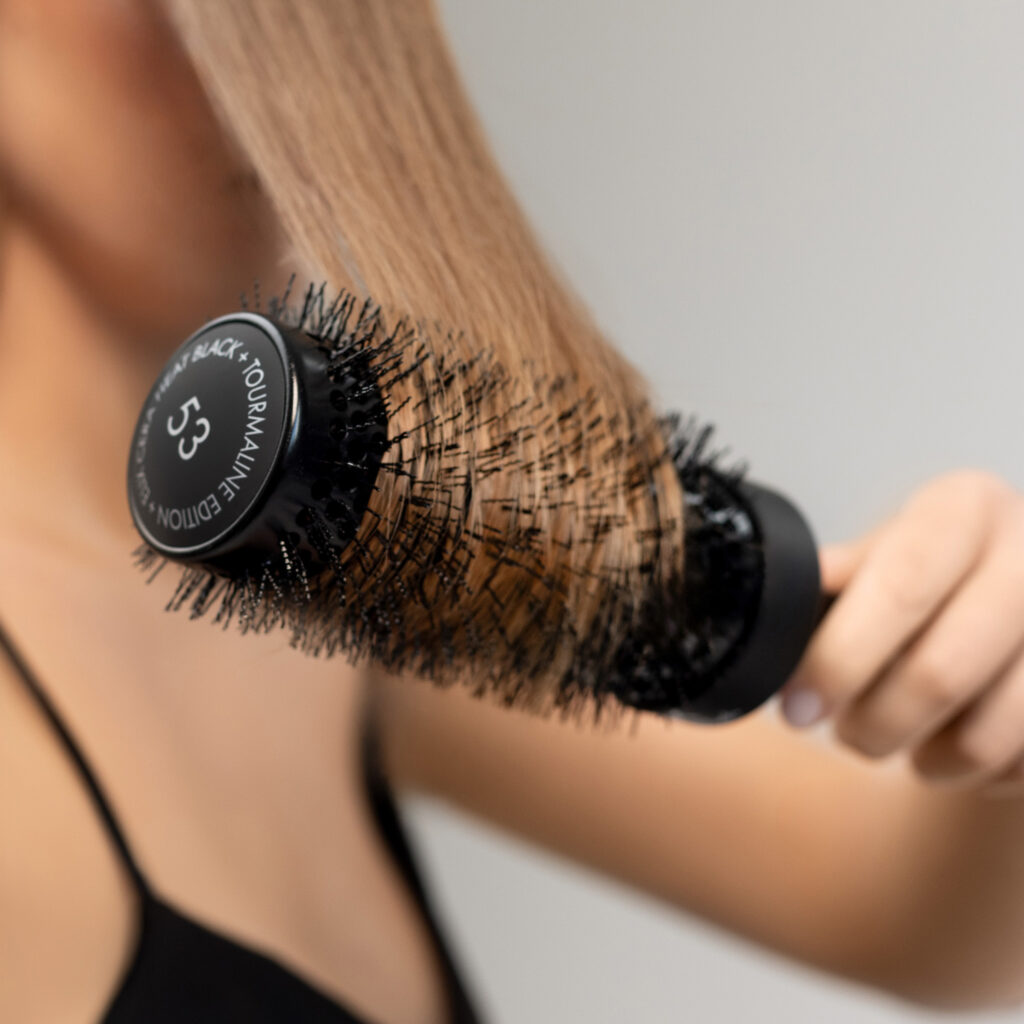 Pasmo włosów modelki nawinięte na czarną okrągłą szczotkę Sister Young ELIX CERA HEAT BLACK+.