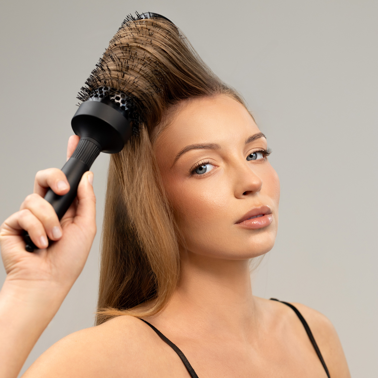 Modelka unosząca włosy u nasady czarną okrągłą szczotką Sister Young ELIX CERA HEAT BLACK+.