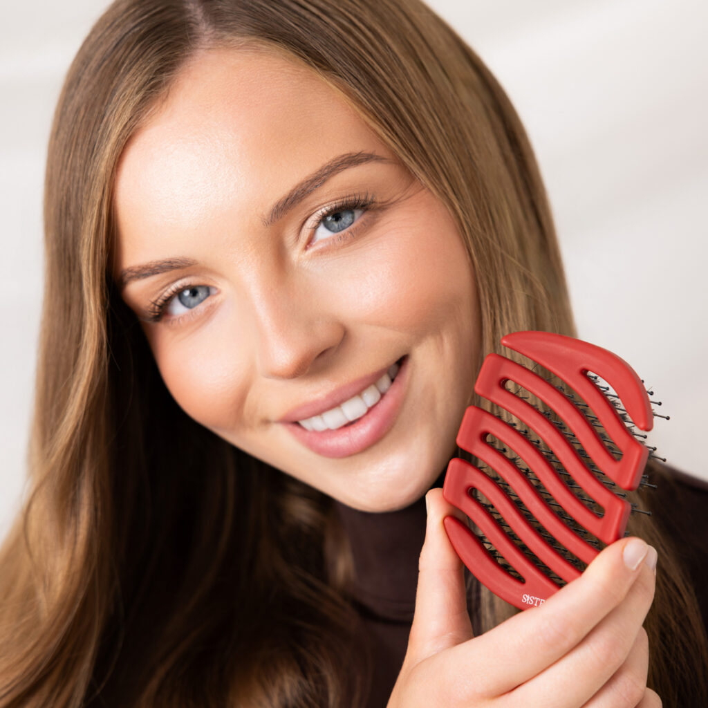 Uśmiechnięta modelka trzymająca przy policzku czerwoną szczotkę Sister Young MILA Cherry Red.