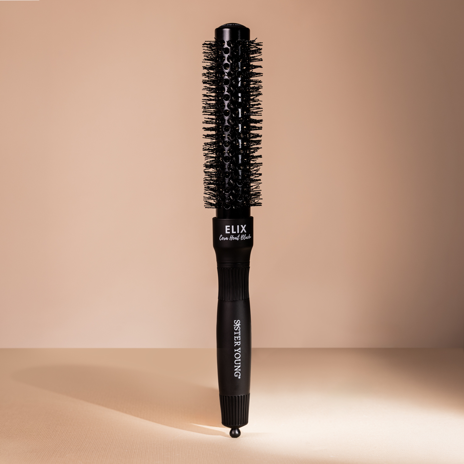 Czarna okrągła szczotka do włosów Sister Young ELIX Cera Heat Black+ 25 mm na beżowym tle