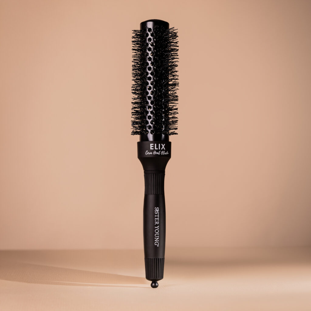 Czarna okrągła szczotka do modelowania Sister Young ELIX BLACK+ 32 mm stojąca na beżowym tle